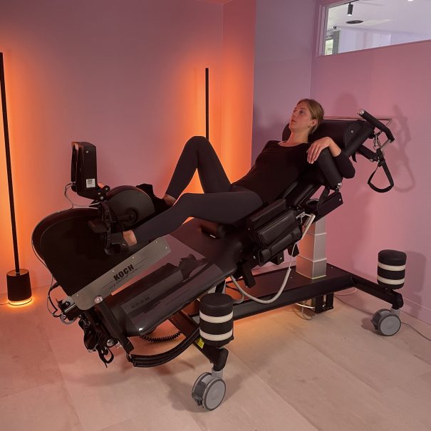 Vue 3/4 du divan d'effort ULKE avec ergomètre intégré et patient – Koch Evolution