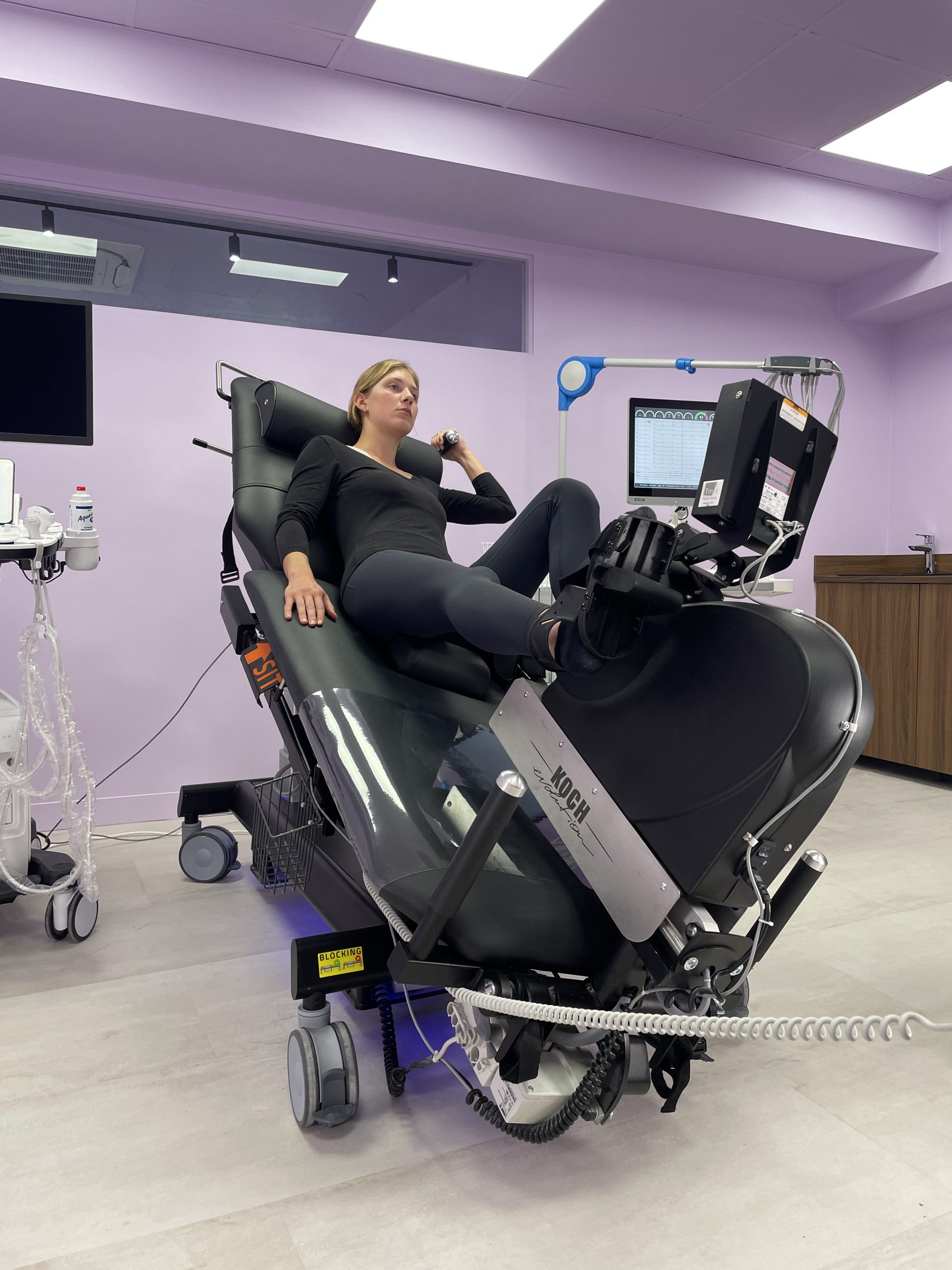 divan ergométrique d'échocardiographie en position d'effort latérale avec un patient se maintenant à la poignée de maintien et utilisant l'ergomètre.